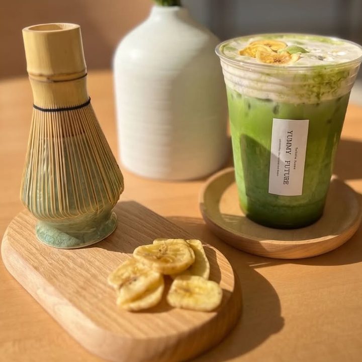 Matcha Banana Einspanner beside a bamboo whisk and banana chips